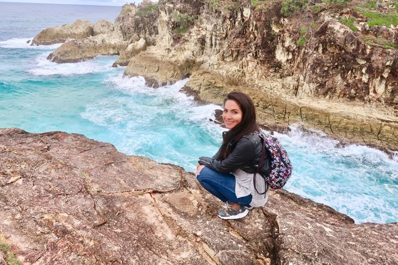 estudiante morena con mochila y arrodillada en una roca en la isla Stradbroke de Australia